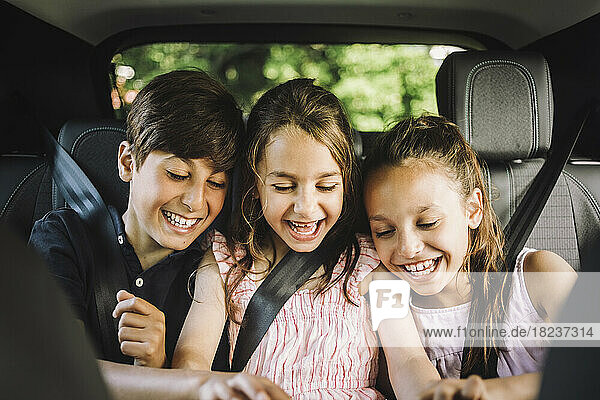 Happy male and female siblings wearing seat belt while enjoying in car