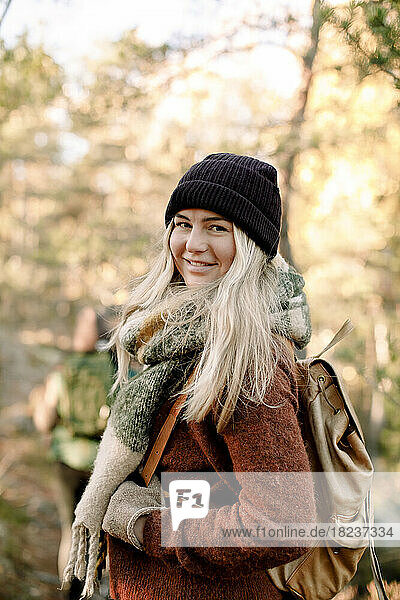 Seitenansicht einer lächelnden jungen Frau mit Rucksack im Wald