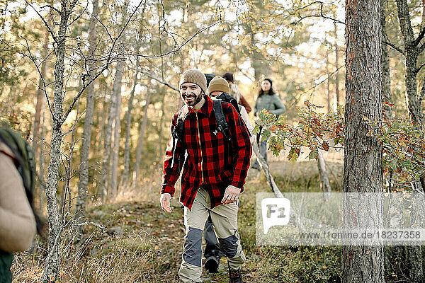 Lächelnder Mann beim Wandern mit Freunden inmitten von Bäumen im Wald