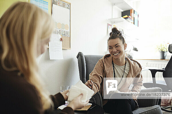 Happy non-binary counselor discussing with female student holding sanitary pads in school office