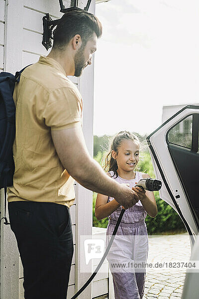 Side view of father teaching daughter to charge electric car