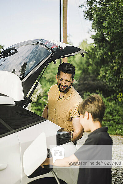 Lächelnder Vater steht neben seinem Sohn und lädt sein Elektroauto auf