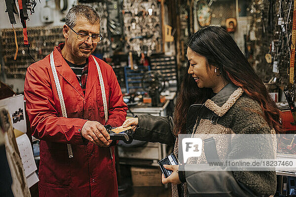 Lächelnde junge Kundin beim kontaktlosen Bezahlen mit Kreditkarte in einer Werkstatt