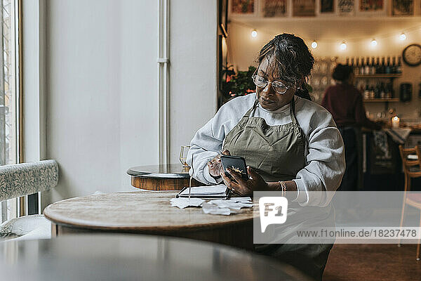 Ältere Frau  die ein Mobiltelefon benutzt  während sie mit einem Tagebuch am Tisch eines Cafés sitzt