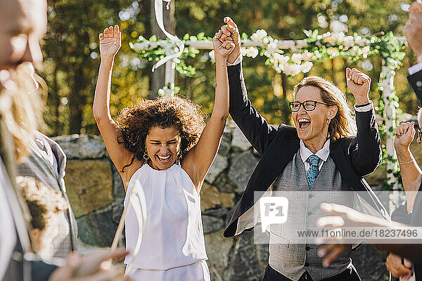 Glückliches lesbisches Paar hält sich an den Händen und tanzt inmitten von Familie und Freunden während der Hochzeitsfeier