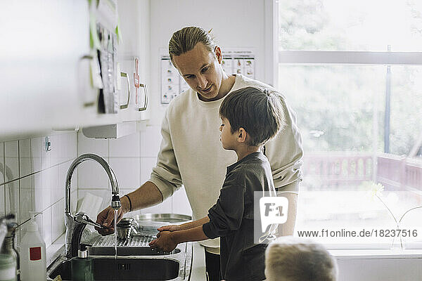 Männlicher Kinderbetreuer bringt einem Jungen in der Nähe des Waschbeckens eines Kindergartens das Händewaschen bei