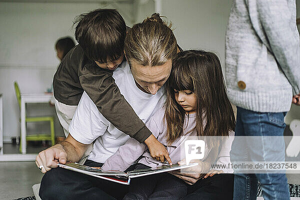 Junge  der auf ein Bilderbuch zeigt  während ein männlicher Lehrer ihm im Kindergarten eine Geschichte erzählt