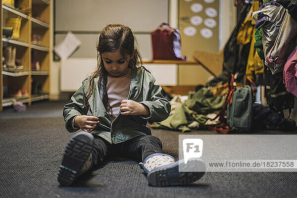 Mädchen mit Jacke sitzt auf Teppich in Kindertagesstätte