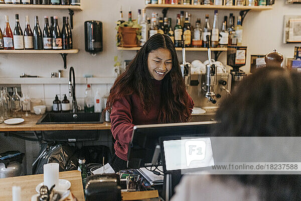Smiling young female owner taking order from customer in cafe