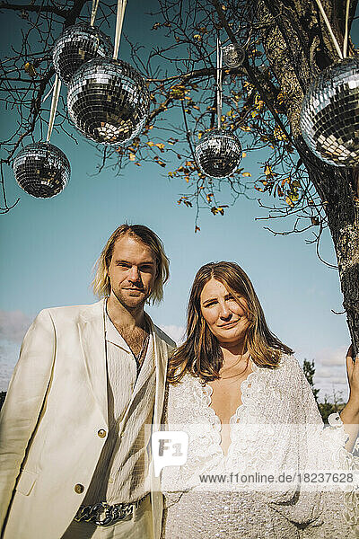 Porträt der neu verheirateten Mitte erwachsenen Bräutigam und Braut stehen unter Disco-Kugeln auf sonnigen Tag