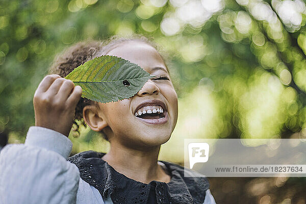 Smiling girl looking through hole in green leaf