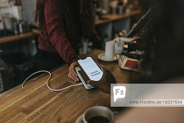 Hand einer Kundin beim kontaktlosen Bezahlen mit dem Smartphone an der Kasse eines Cafés