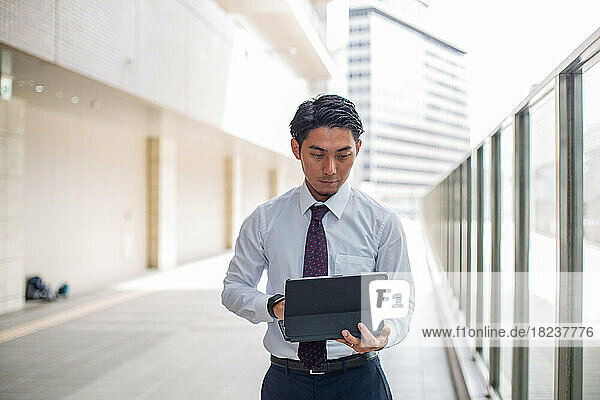 A young businessman in the city  on the move  standing on a walkway using his laptop.