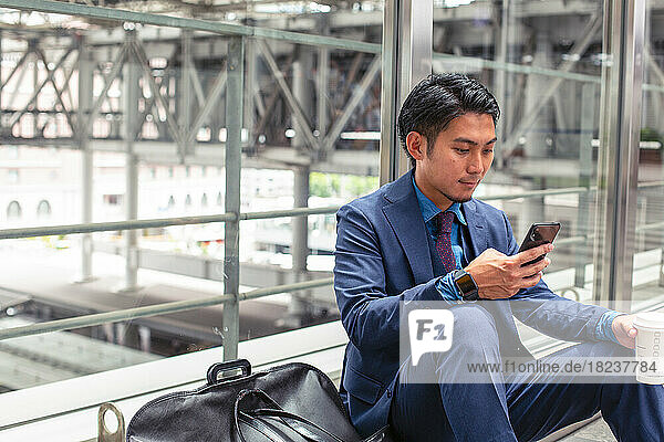 A young businessman in a blue suit in a city  looking at his mobile phone screen  texting or reading a message.