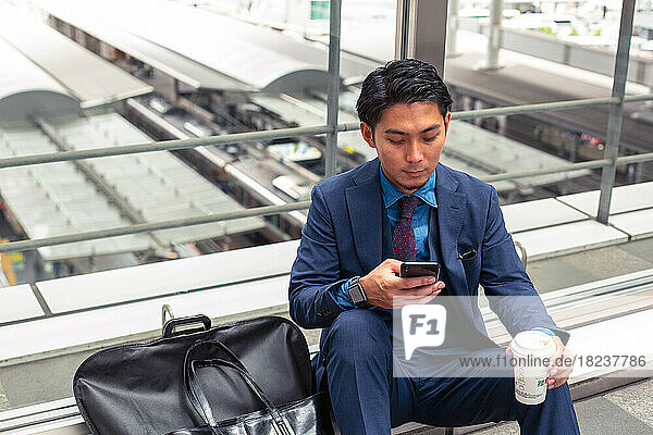 A young businessman in a blue suit in a city  looking at his mobile phone screen  texting or reading a message.