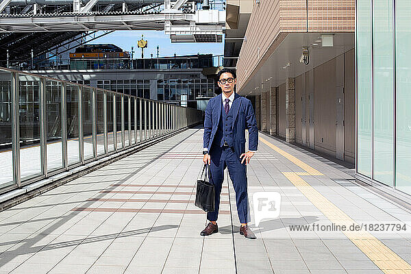 A young businessman in the city  on the move  a man in a suit with a laptop bag  standing legs apart on a walkway.