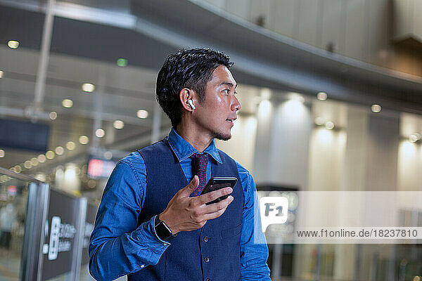A young businessman in the city  on the move  at a transport hub  holding his phone and looking around.