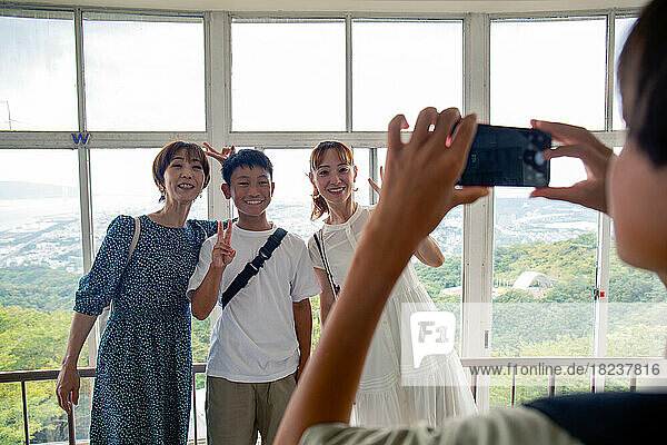 A boy using his mobile phone to take a picture of three people  a 13 year old boy  his mother and a friend.
