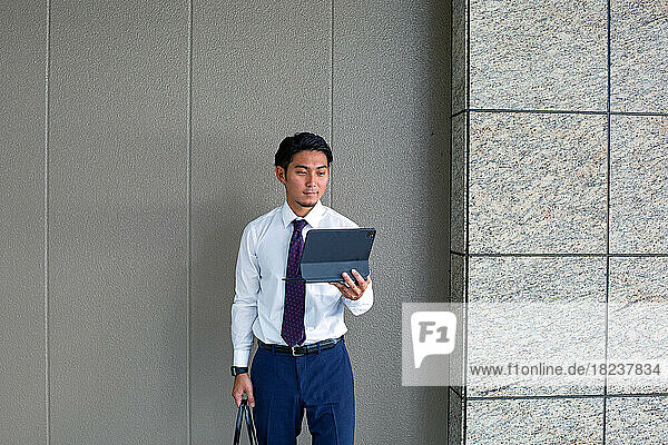 A young businessman in the city  on the move  standing outside a building  holding his laptop.