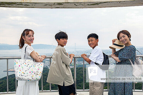 Four Japanese people on a outing  two mature women and two 13 year old boys  in a row  on a viewing platform.