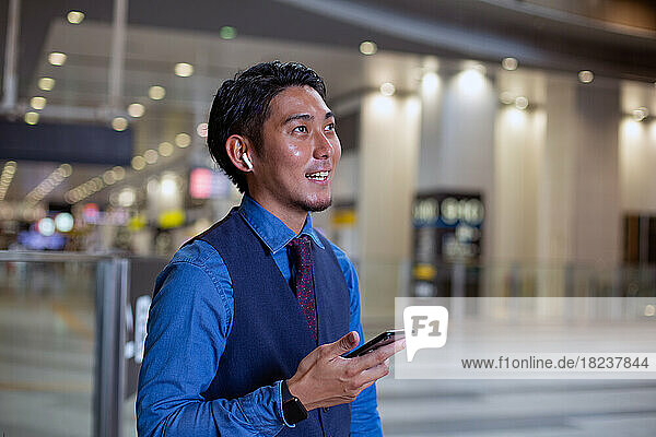 A young businessman in the city  standing looking around  holding his mobile phone.