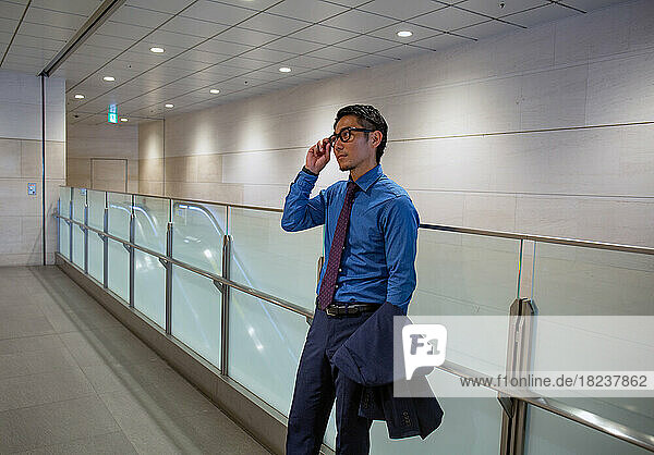A young businessman in the city  on the move  in a hallway speaking on his mobile phone.