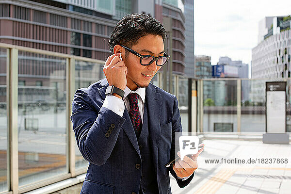 A young businessman in the city  on the move  a man in a suit outside  holding a mobile and his ear  using ear buds.