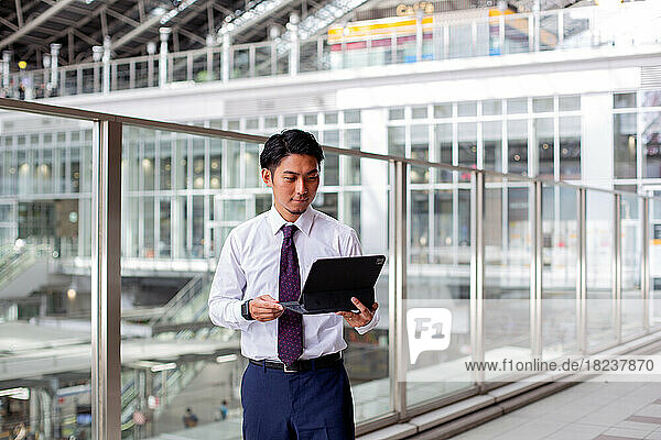 A young businessman in the city  on the move  standing on a walkway holding his laptop and using the screen.