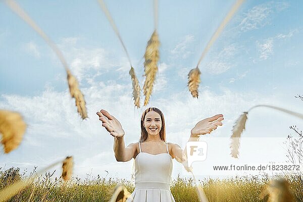Glückliche junge Frau streckt ihre Hände nach den Weizenähren aus