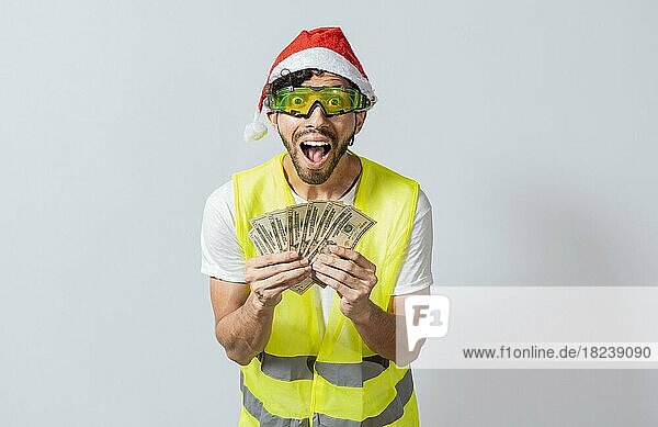 Ingenieur in Weihnachtsmütze hält Geld lächelnd in die Kamera. Bauunternehmer Ingenieur in Weihnachtsmütze mit glücklichen Ausdruck hält Dollar isoliert. Konzept der Ingenieur mit Geld in der Ferienzeit