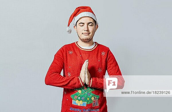 Kerl mit Händen zusammen beten in Weihnachten isoliert  Konzept der Person mit Weihnachtsmütze beten und einen Wunsch zu machen. Mann mit Weihnachtsmütze mit betenden Händen isoliert