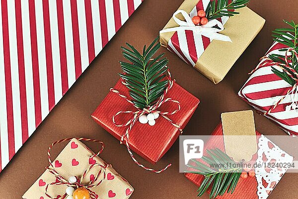 Draufsicht auf schöne rot  weiß und natürlich braun dekoriert Weihnachtsgeschenk-Boxen mit Bändern und Tannenzweigen auf braunem Hintergrund