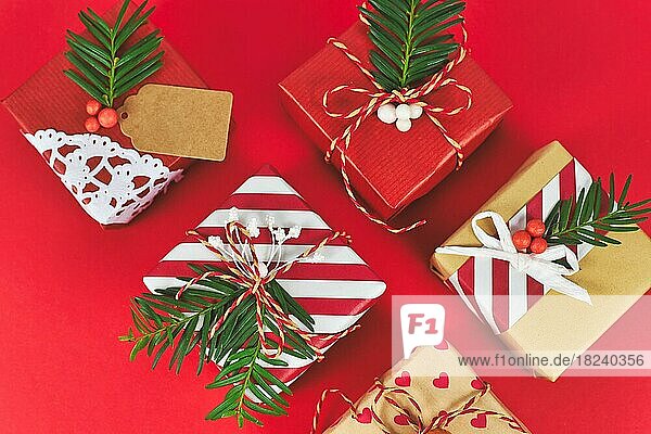 Draufsicht auf schöne rot  weiß und natürlich braun dekoriert Weihnachtsgeschenk-Boxen mit Bändern und Tannenzweigen auf rotem Hintergrund