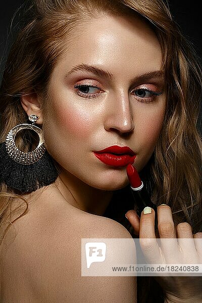 Schönes Mädchen mit roten Lippen und klassischen Make-up und Locken mit Lippenstift in der Hand. Schönes Gesicht. Foto im Studio aufgenommen