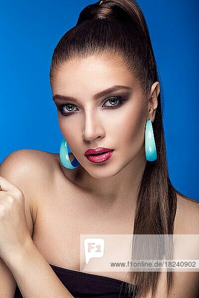 Beautiful woman with evening make-up  bright accessories and long straight hair  Smoky eyes. Fashion photo. Picture taken in the studio on a blue background