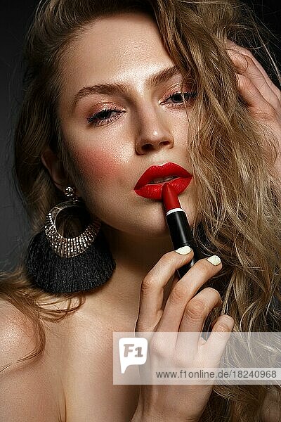 Beautiful girl with red lips and classic makeup and curls with lipstick in hand. Beauty face. Photo taken in the studio