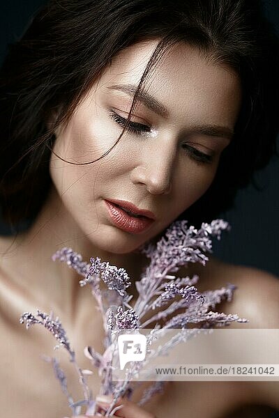Schöne Frau mit einem leichten natürlichen Make-up und perfekter Haut mit Blumen in der Hand. Schönes Gesicht. Bild im Studio auf einem schwarzen Hintergrund aufgenommen