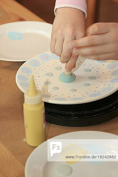 Ein Kind bemalt und verziert einen Teller mit einem Schaumstoffstempel