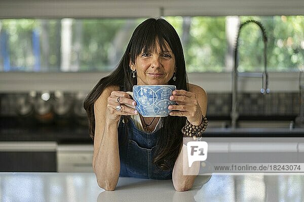 Porträt einer lächelnden Frau  die eine entspannende Kaffeepause zu Hause genießt und in die Kamera schaut