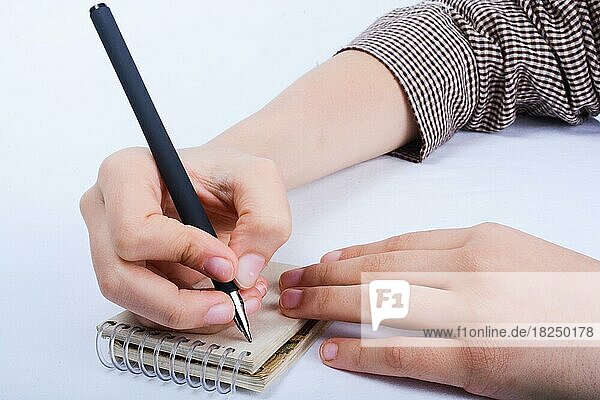 Ein Kind Hand ist das Schreiben mit Stift auf einer Spirale Notebook auf weißem Hintergrund