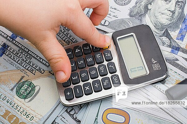 Toddler is holding calculator on the banknote of US dollars spread around