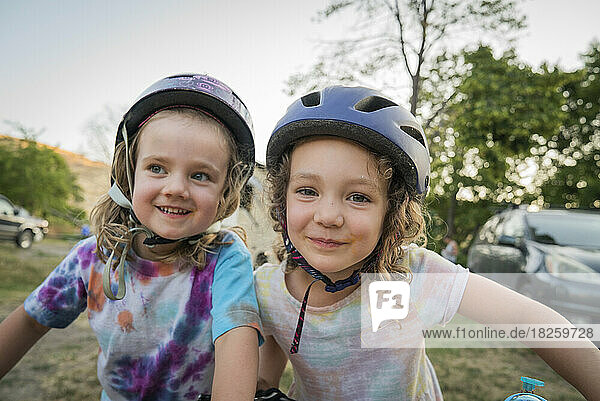 Two young girls in bike helmets smile for camera