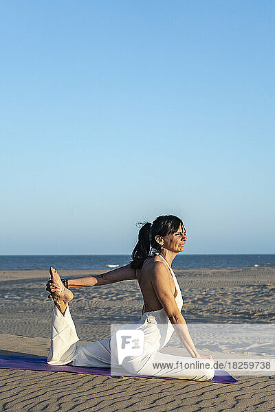 A woman practicing yoga on a mat on the beach next to the ocean