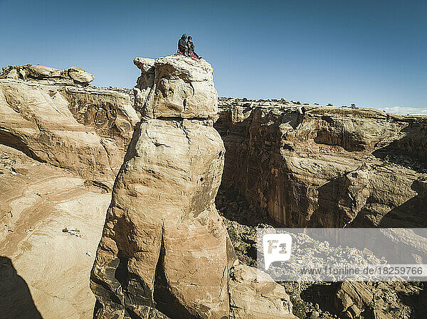 Man and woman sitting on rock tower at Bride Canyon against clear sky