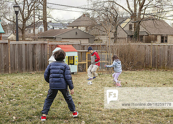 A father plays soccer with children in yard by chicken coop