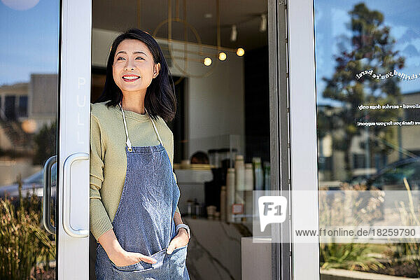 Smiling female entrepreneur leaning on doorway of cafe