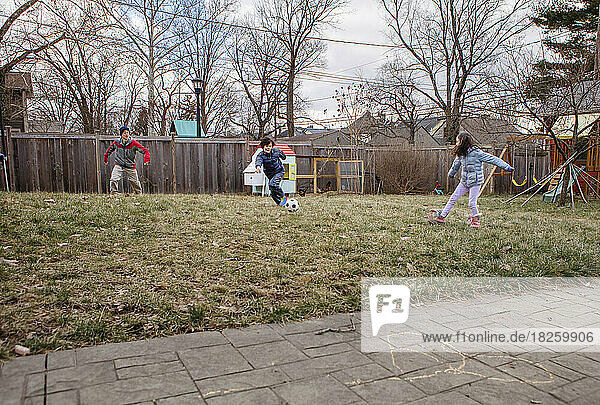 A boy plays soccer with his family in suburban backyard in winter