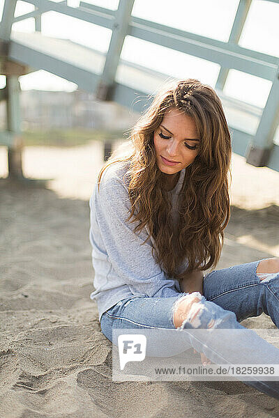 Beautiful young woman sitting alone on beach in california