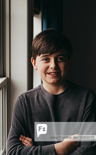 Portrait of happy smiling tween boy standing beside a window.