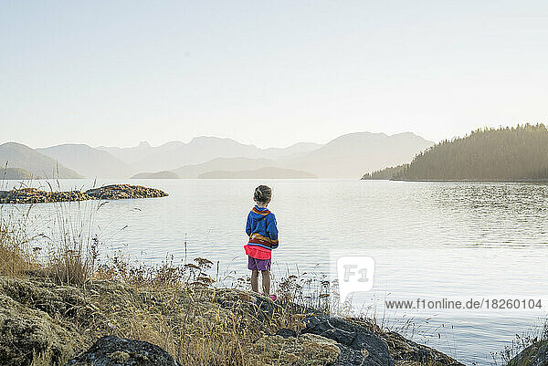 A young girl stands at the edge of a rock island at sunrise
